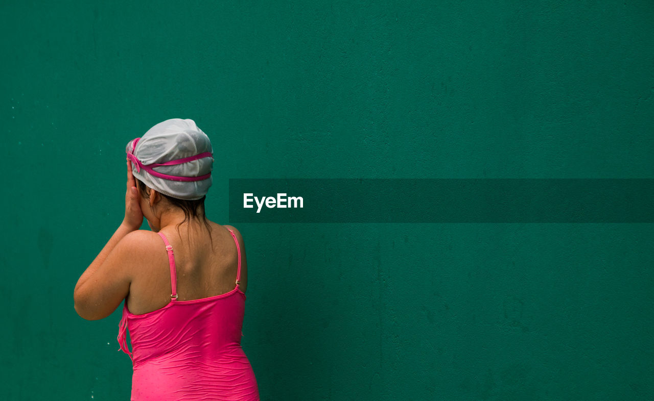 Rear view of wet girl standing against wall