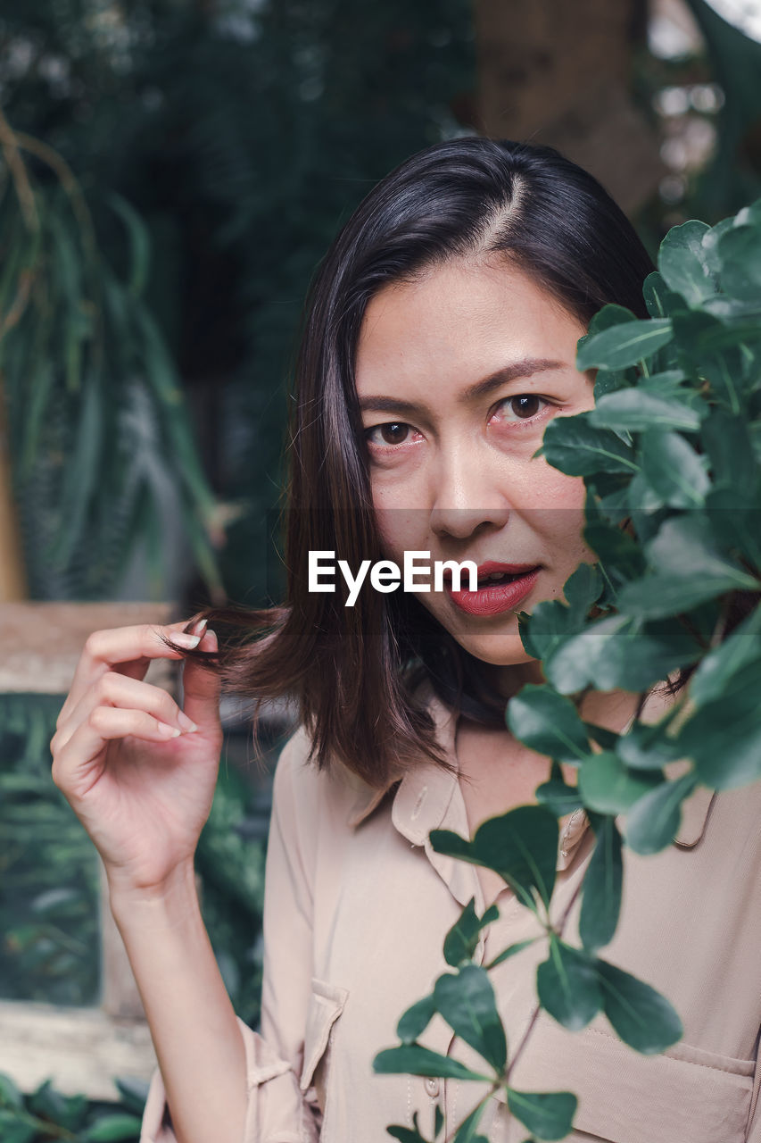 PORTRAIT OF YOUNG WOMAN HOLDING PLANT