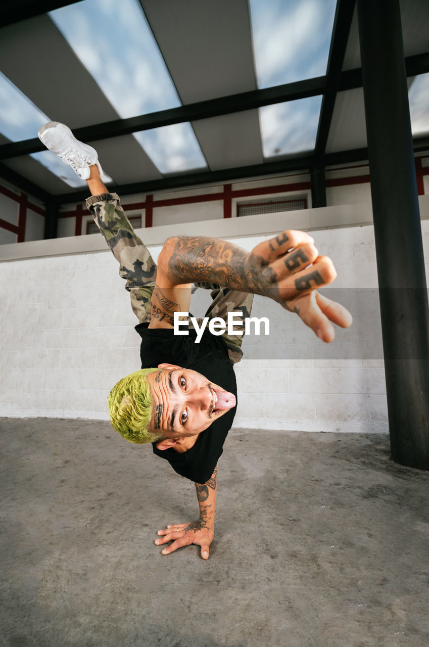 Full body of energetic young man doing acrobatic handstand while performing break dance