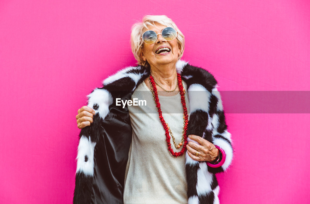 Portrait of smiling woman standing against pink background