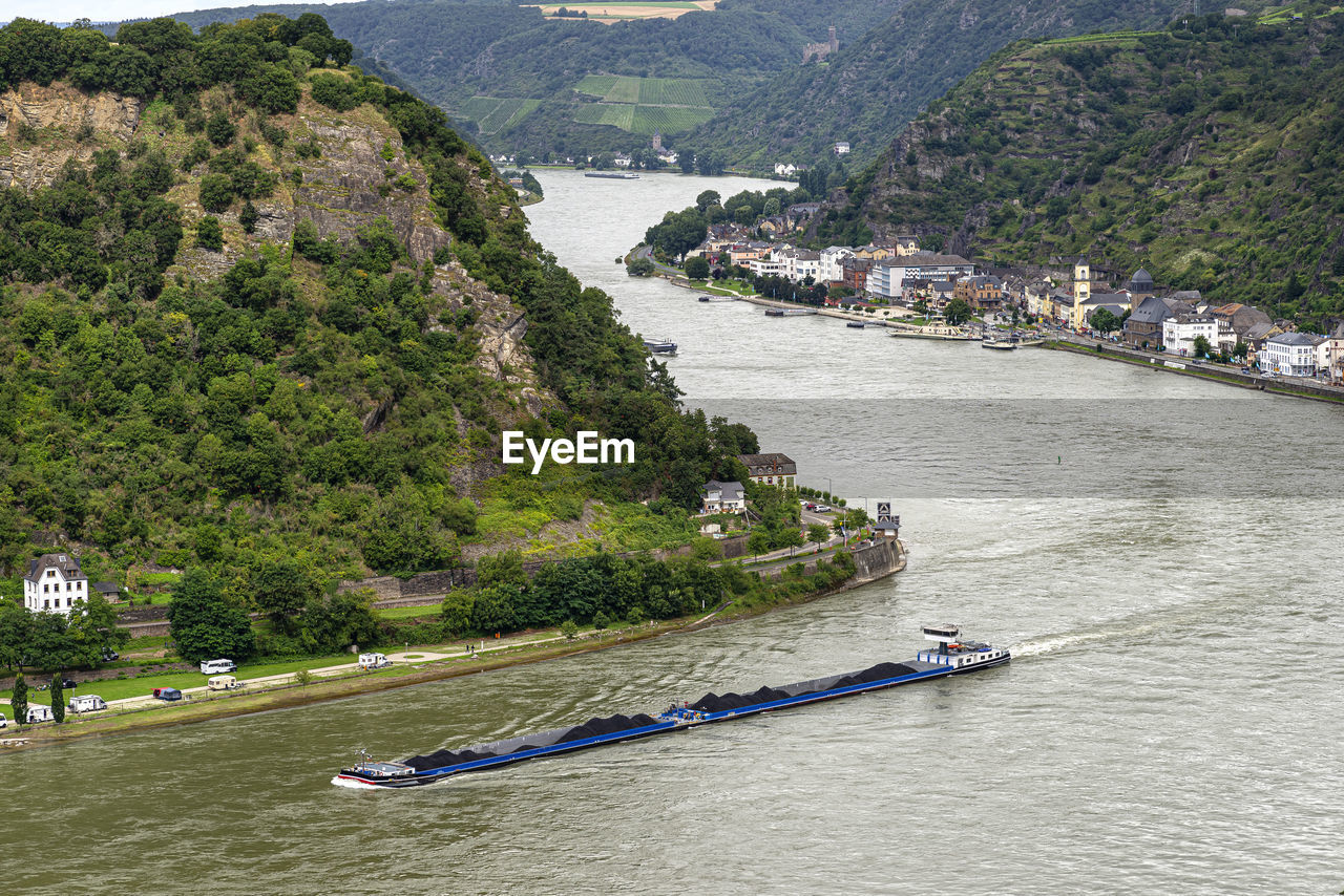 A barge with coal sailing on the river rhine in western germany, visible buildings on the river bank