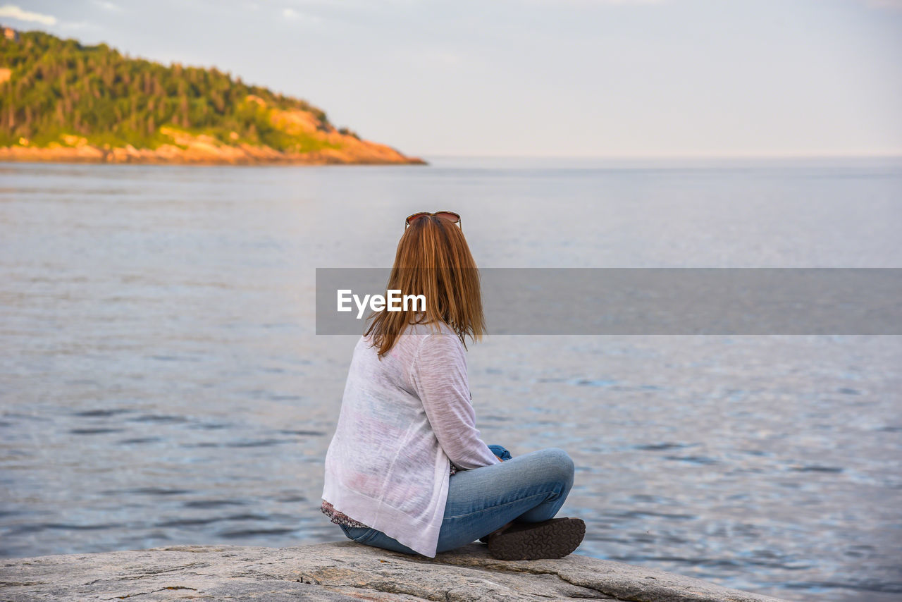 Woman sitting by sea against sky