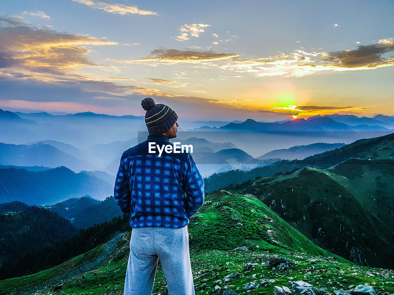 Rear view of man standing on mountain against sky during sunset