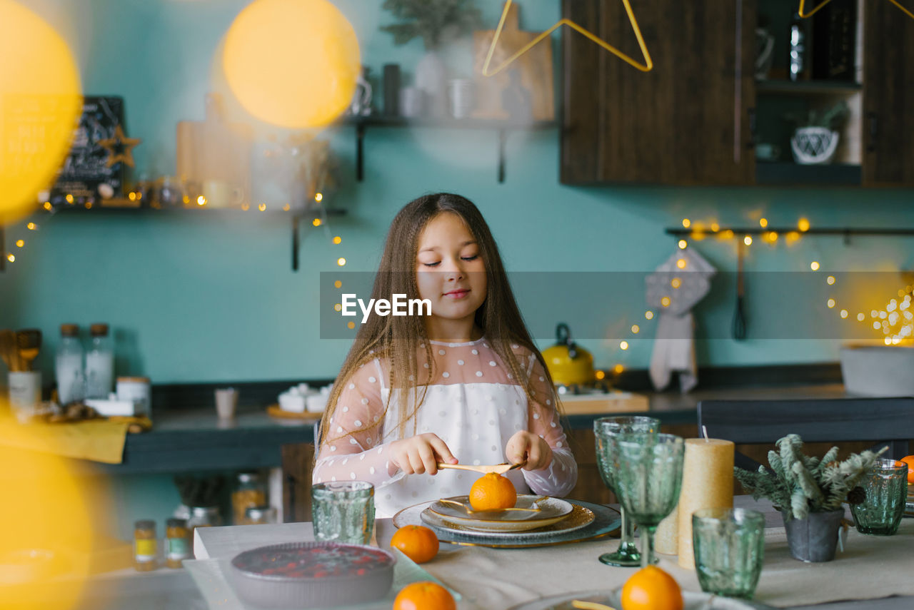 Child girl is sitting at a festive table set for christmas and smiling