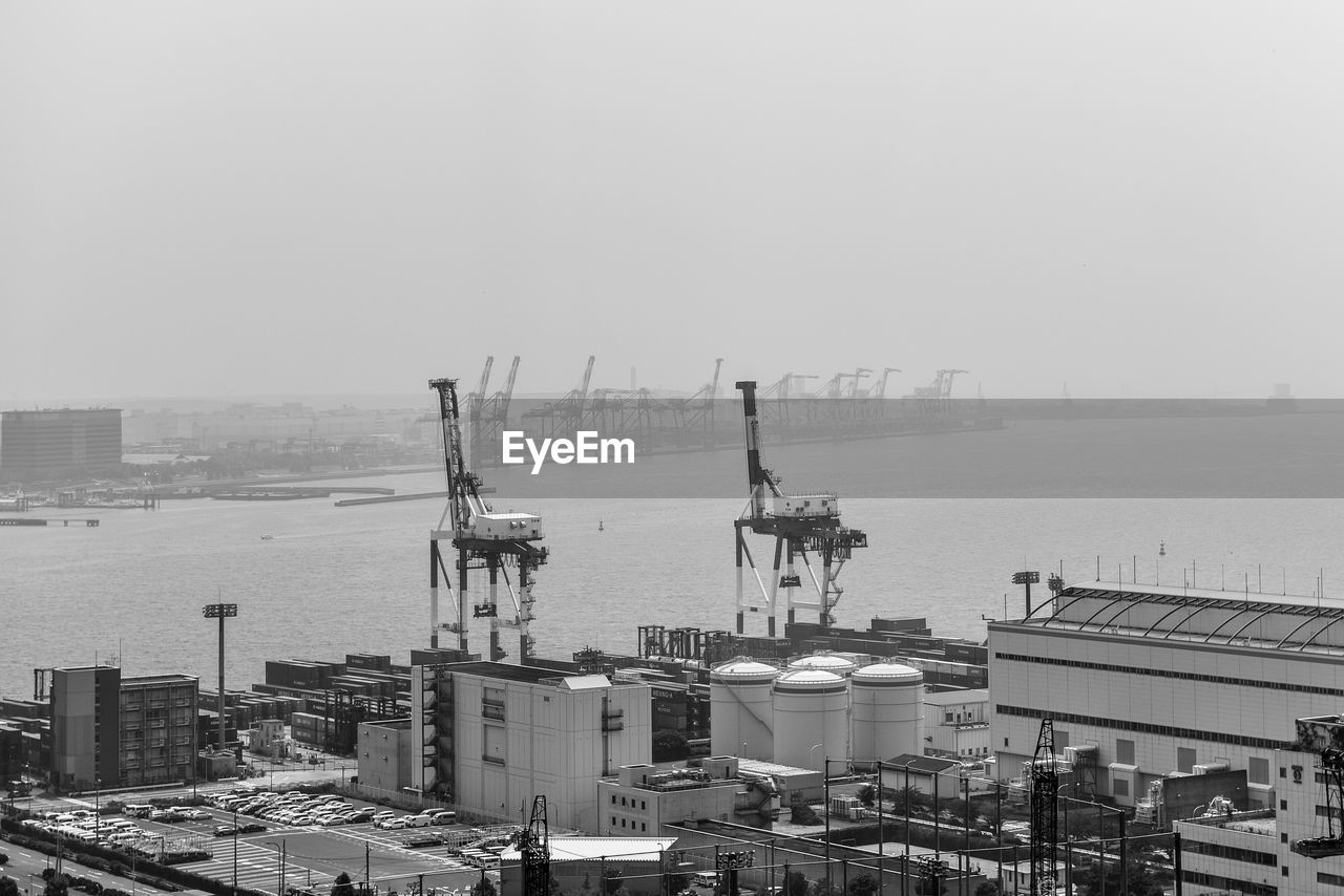 HIGH ANGLE VIEW OF CRANES BY BUILDINGS AGAINST SKY