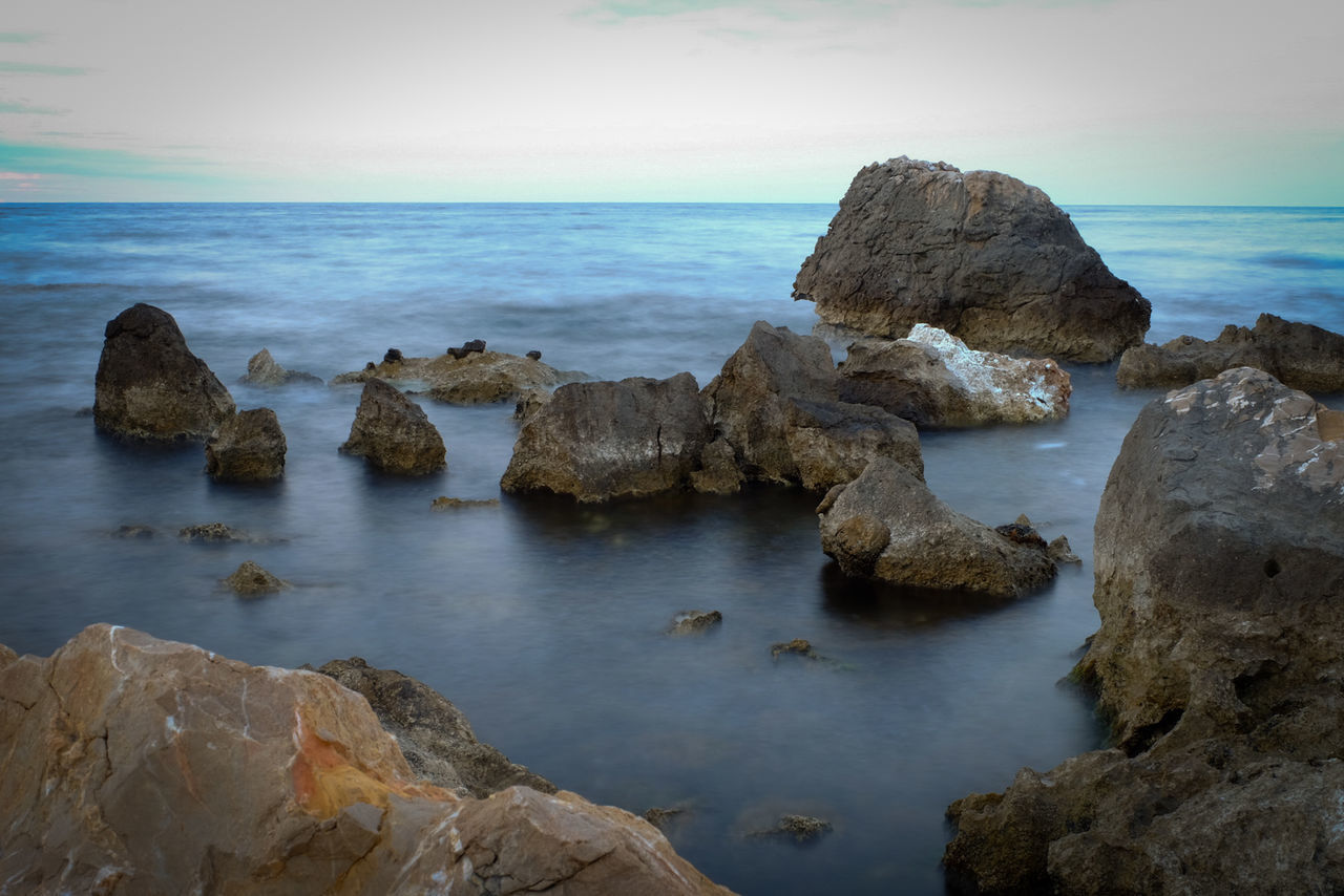 ROCKS BY SEA AGAINST SKY