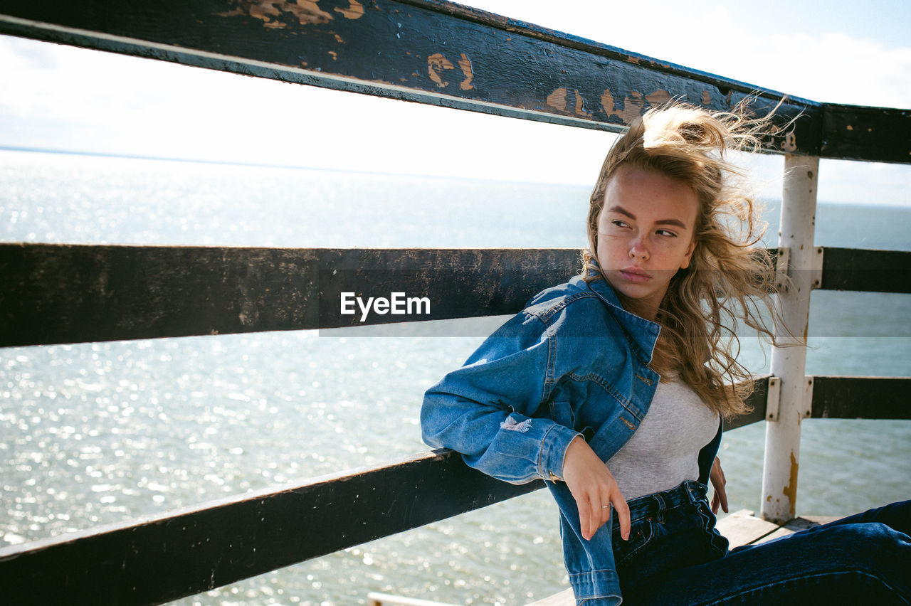 Young woman sitting on pier over sea against sky