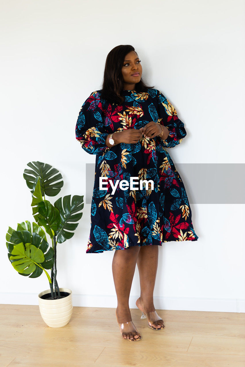 one person, full length, women, dress, indoors, spring, fashion, standing, adult, flower, clothing, houseplant, portrait, flowerpot, female, plant, lifestyles, pattern, front view, nature, potted plant, studio shot, smiling, photo shoot, footwear, person, young adult, hairstyle, flooring, floral pattern