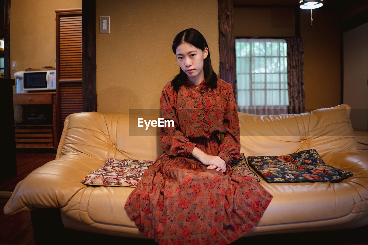 PORTRAIT OF YOUNG WOMAN SITTING ON SOFA AT HOME