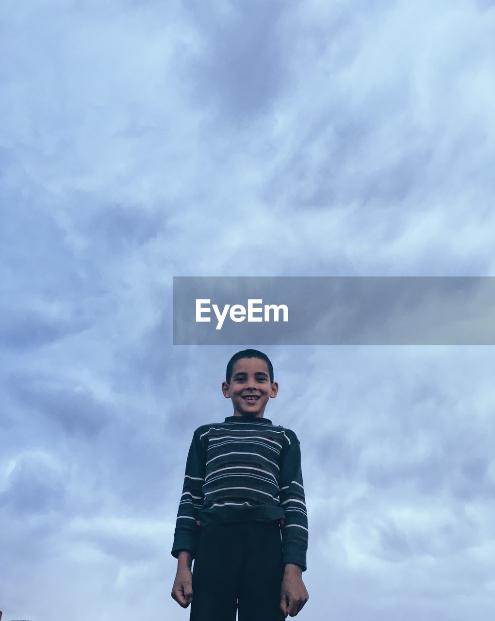 Low angle portrait of smiling boy standing against cloudy sky