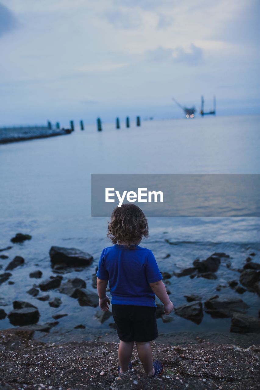 Rear view full length of boy standing on shore at beach