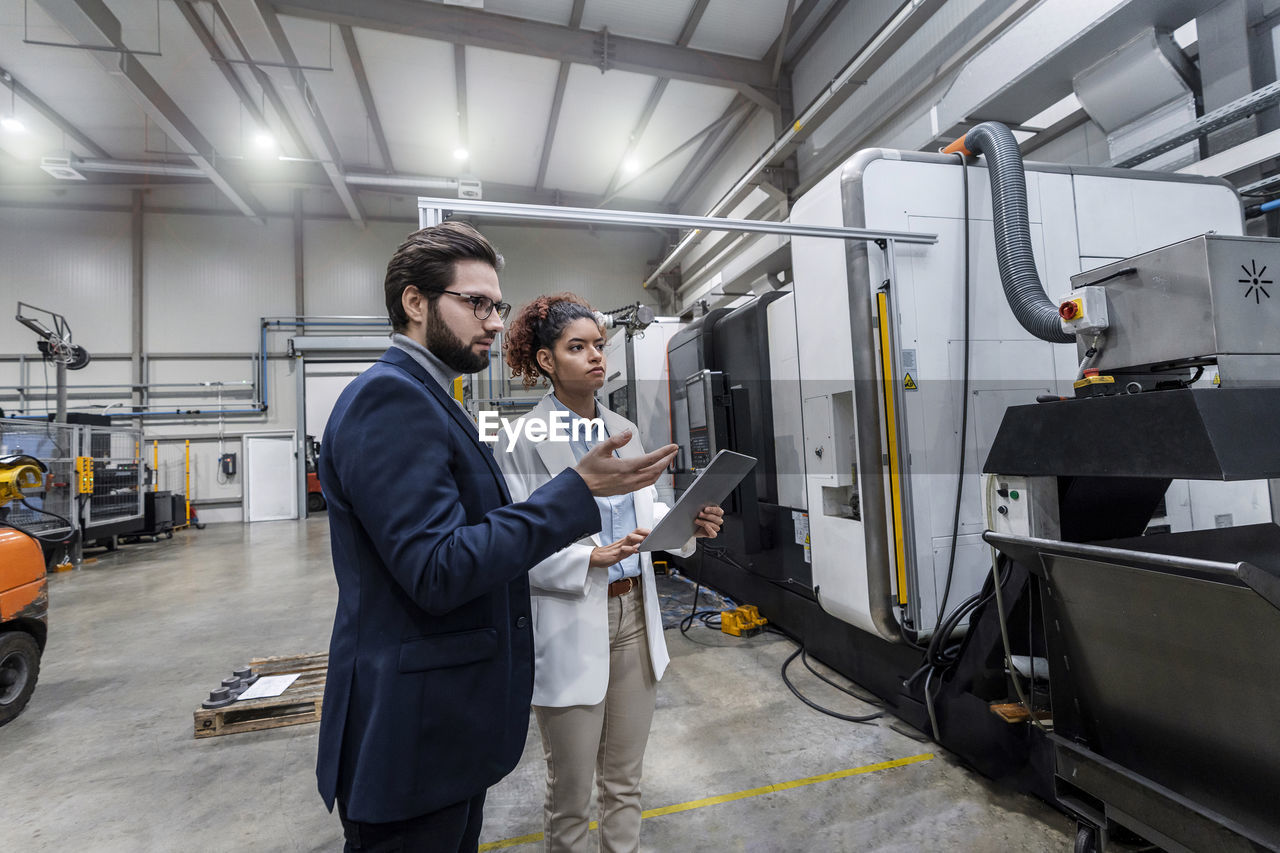 Engineers discussing over machine in factory