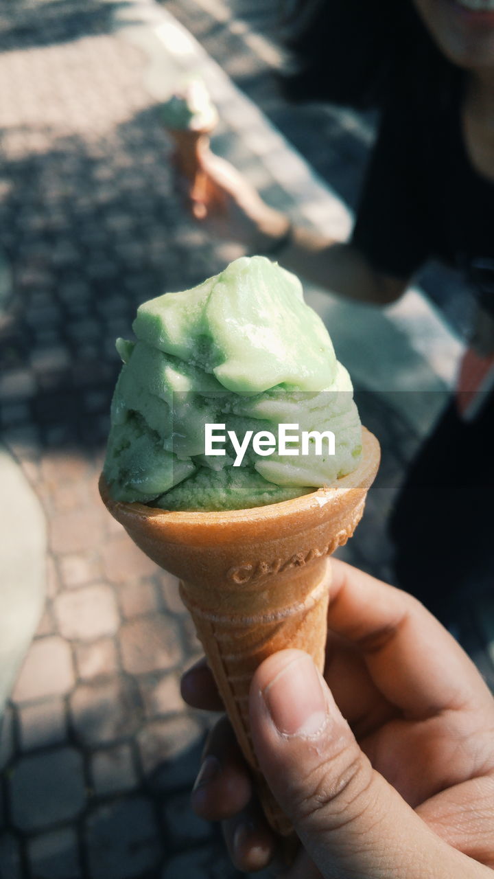 CROPPED IMAGE OF HAND HOLDING ICE CREAM CONE OUTDOORS