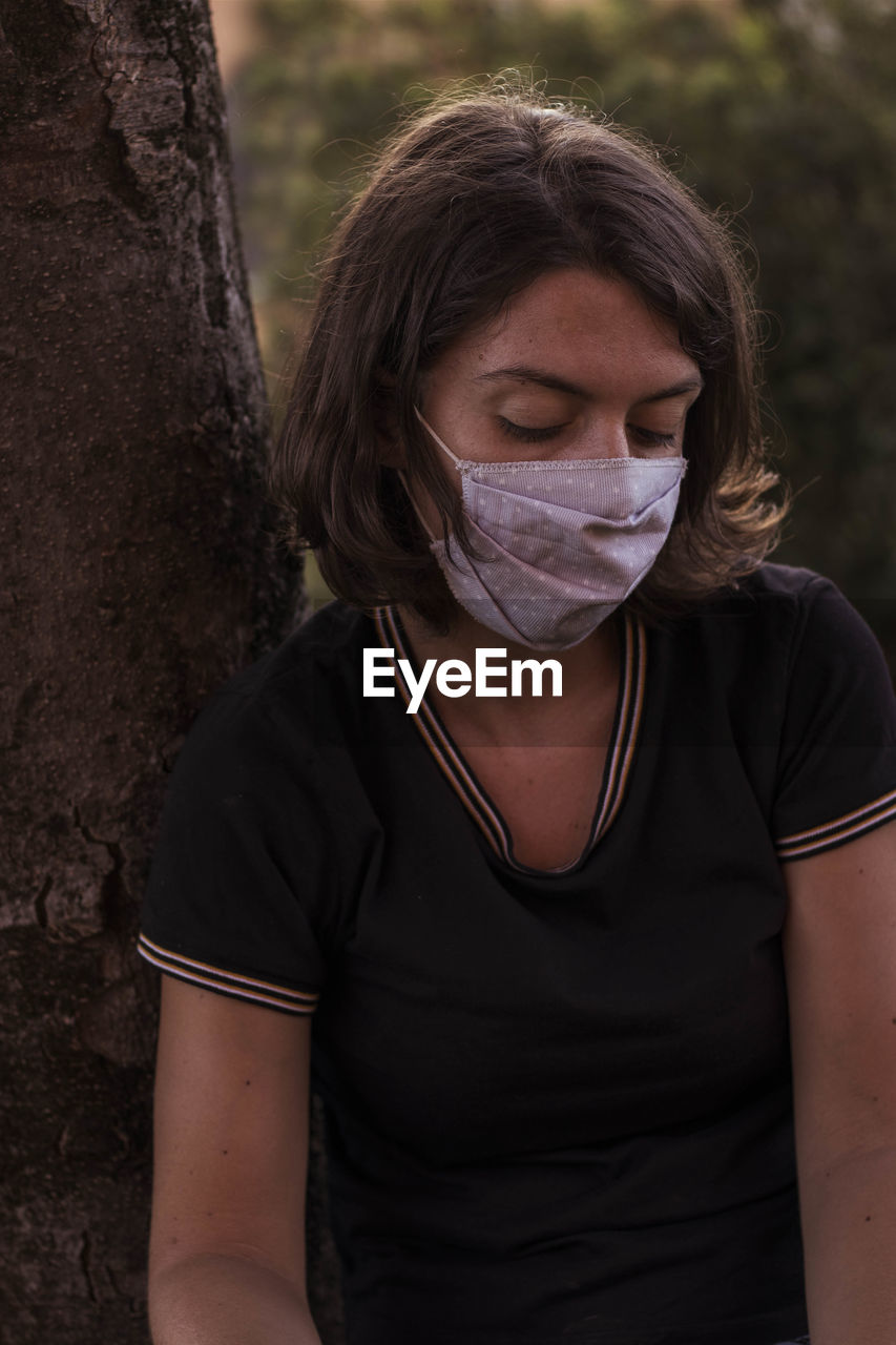 Portrait of young woman with mask standing on tree trunk