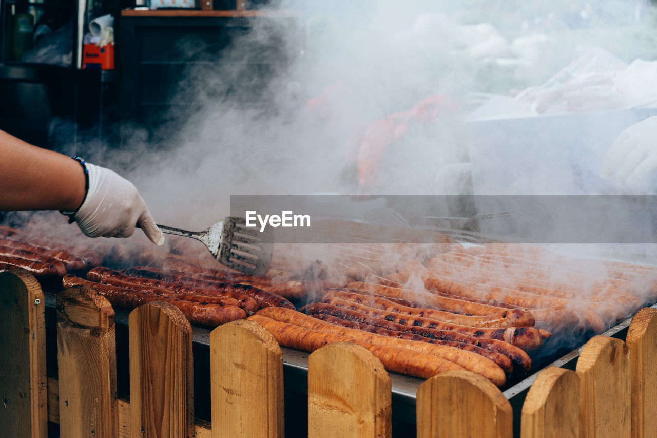 Cropped image of hand cooking sausages on barbecue grill