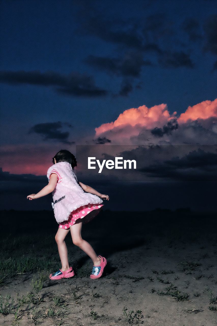 Full length of girl playing on field against cloudy sky at dusk