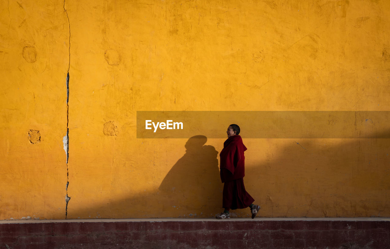 REAR VIEW OF MAN STANDING AGAINST YELLOW WALL