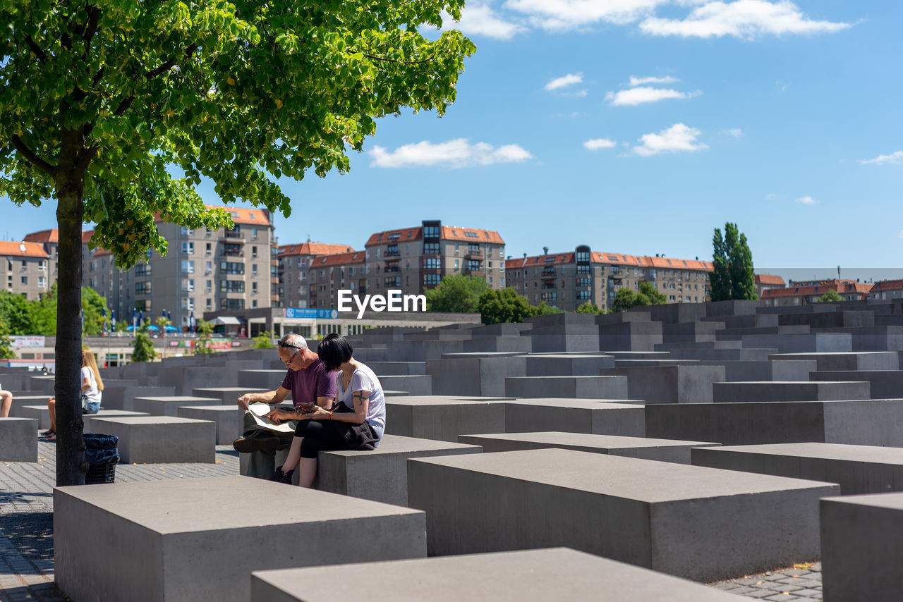 WOMAN SITTING ON BENCH IN CITY AGAINST BUILDINGS