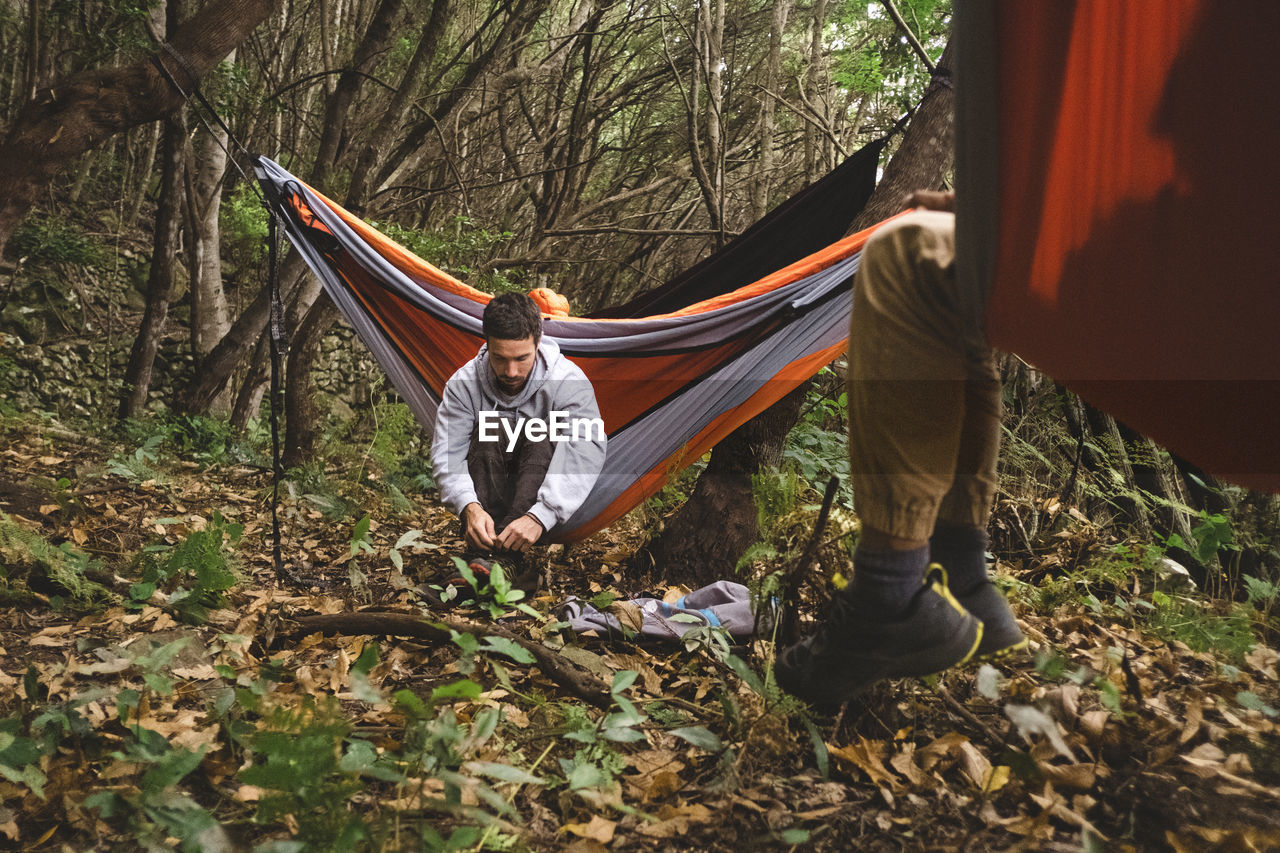 A man sitting in a hammock in the forest gets prepared for hiking