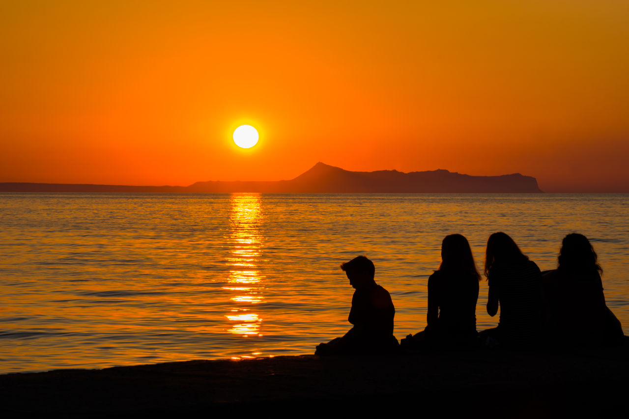 Silhouette friends sitting against sea during sunset