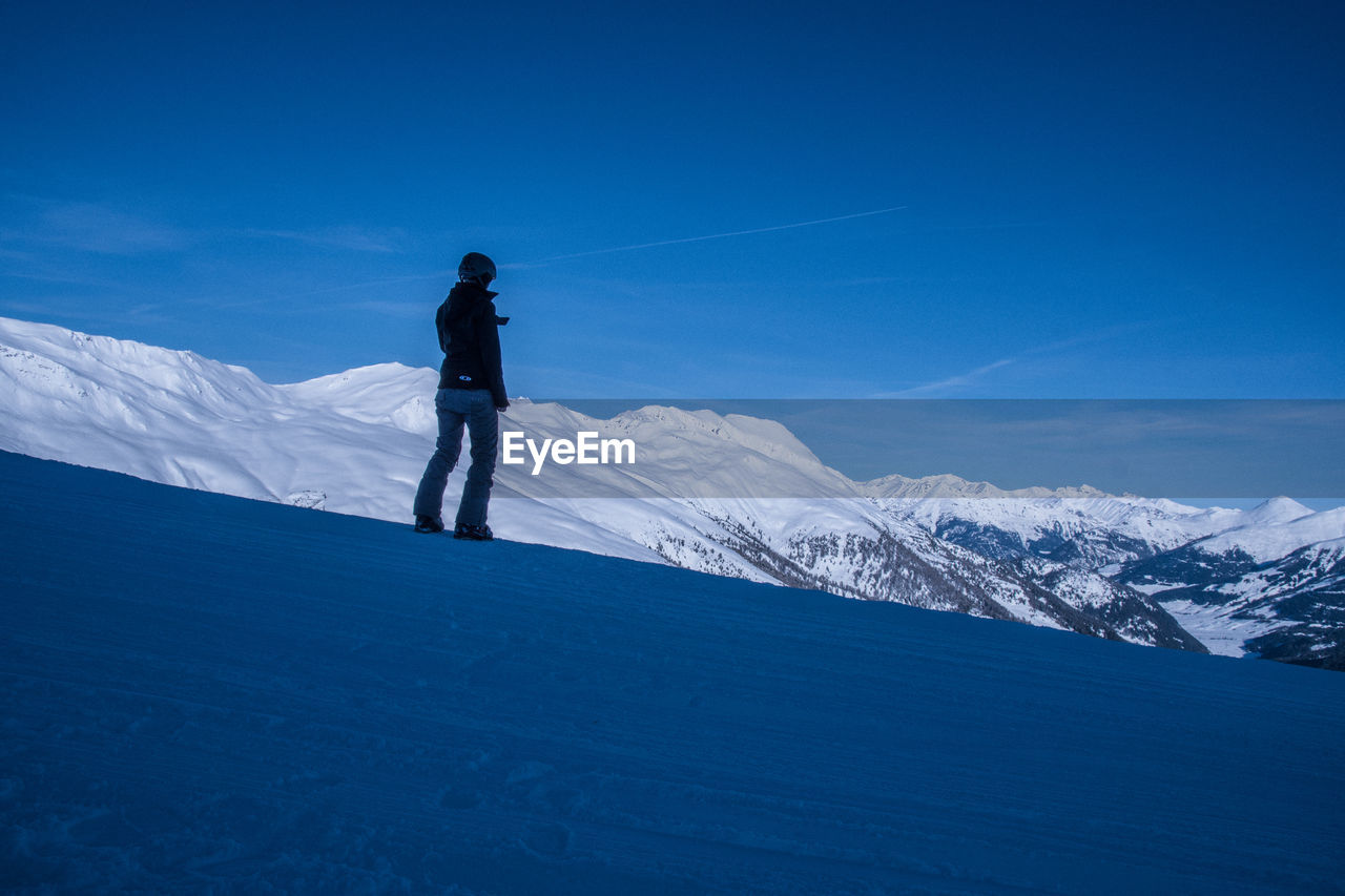 Woman standing on snowcapped mountain against sky