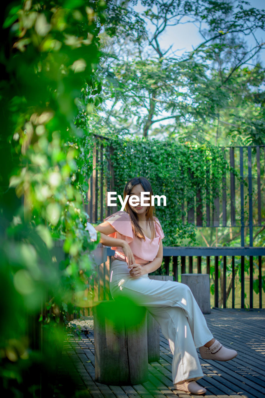 Portrait of young woman sitting on wood against trees