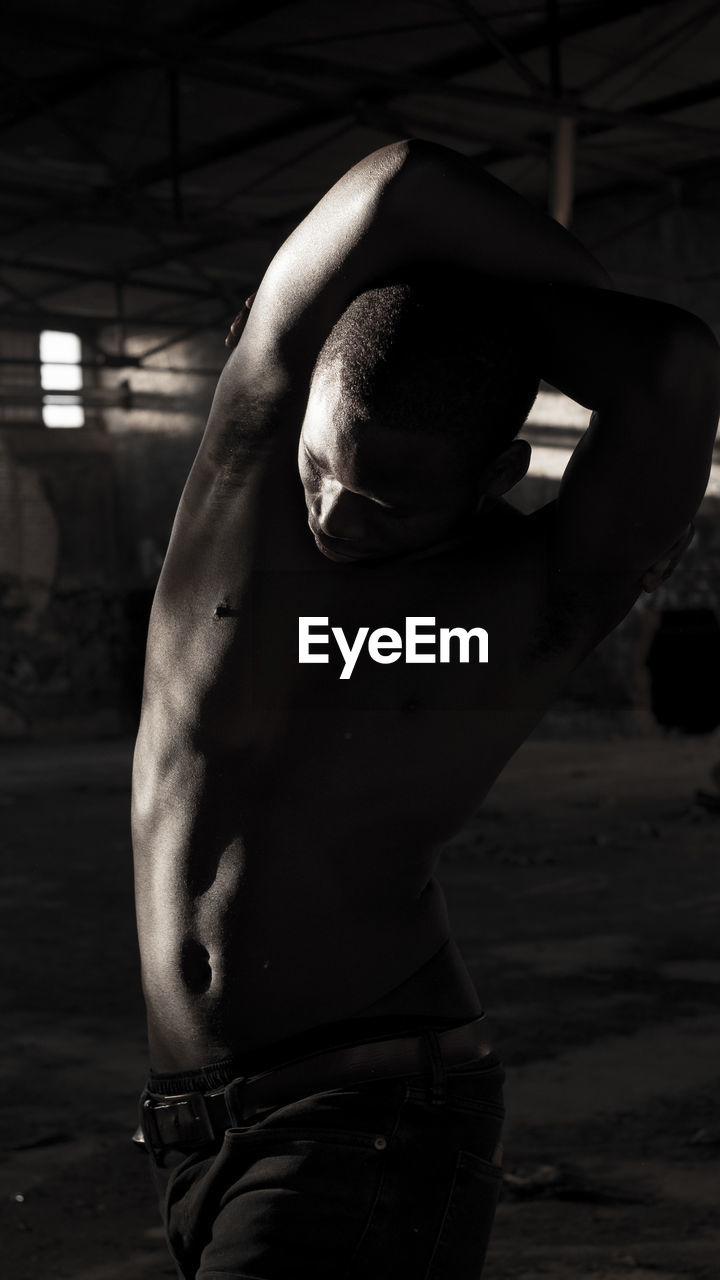 Shirtless man stretching arms in darkroom
