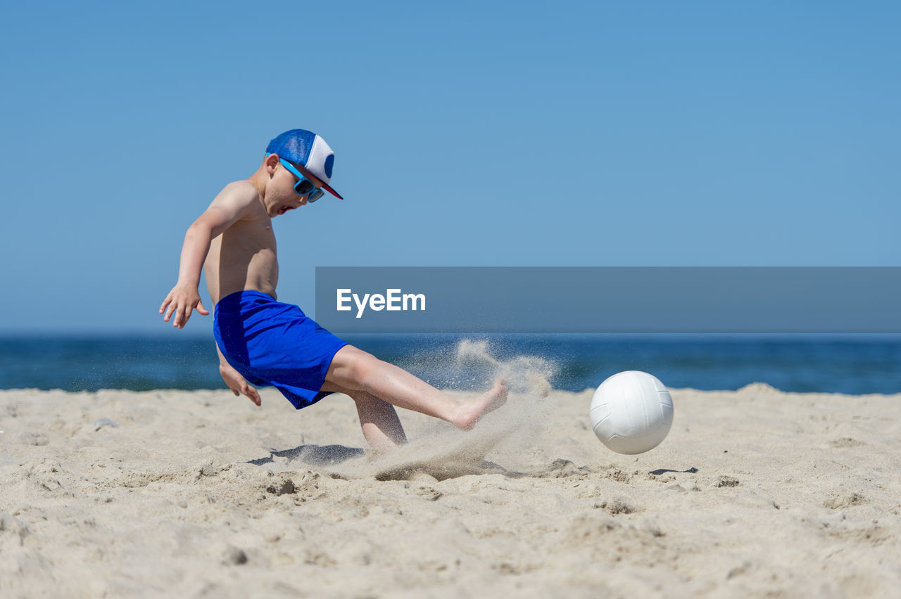 Boy kicking volleyball against sea