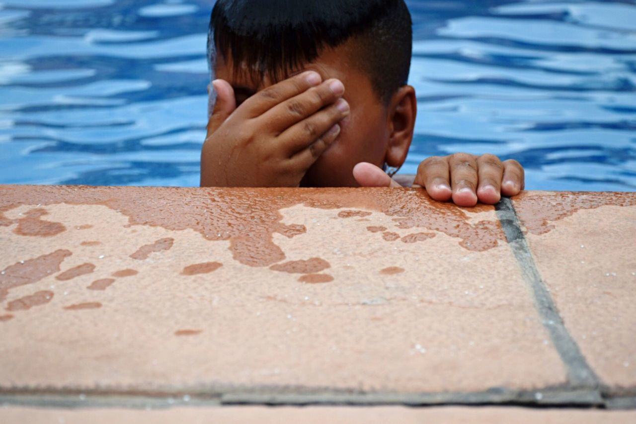 Boy in swimming pool covering his face with hand
