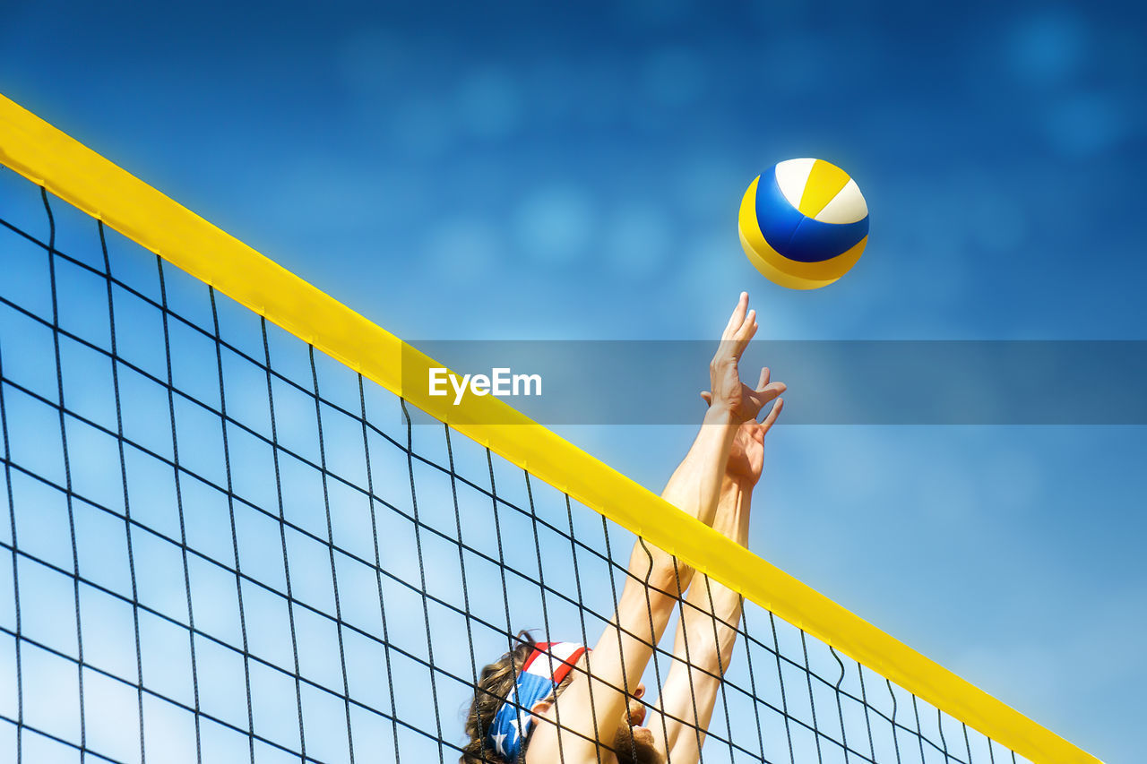 Low angle view of man playing volleyball against blue sky