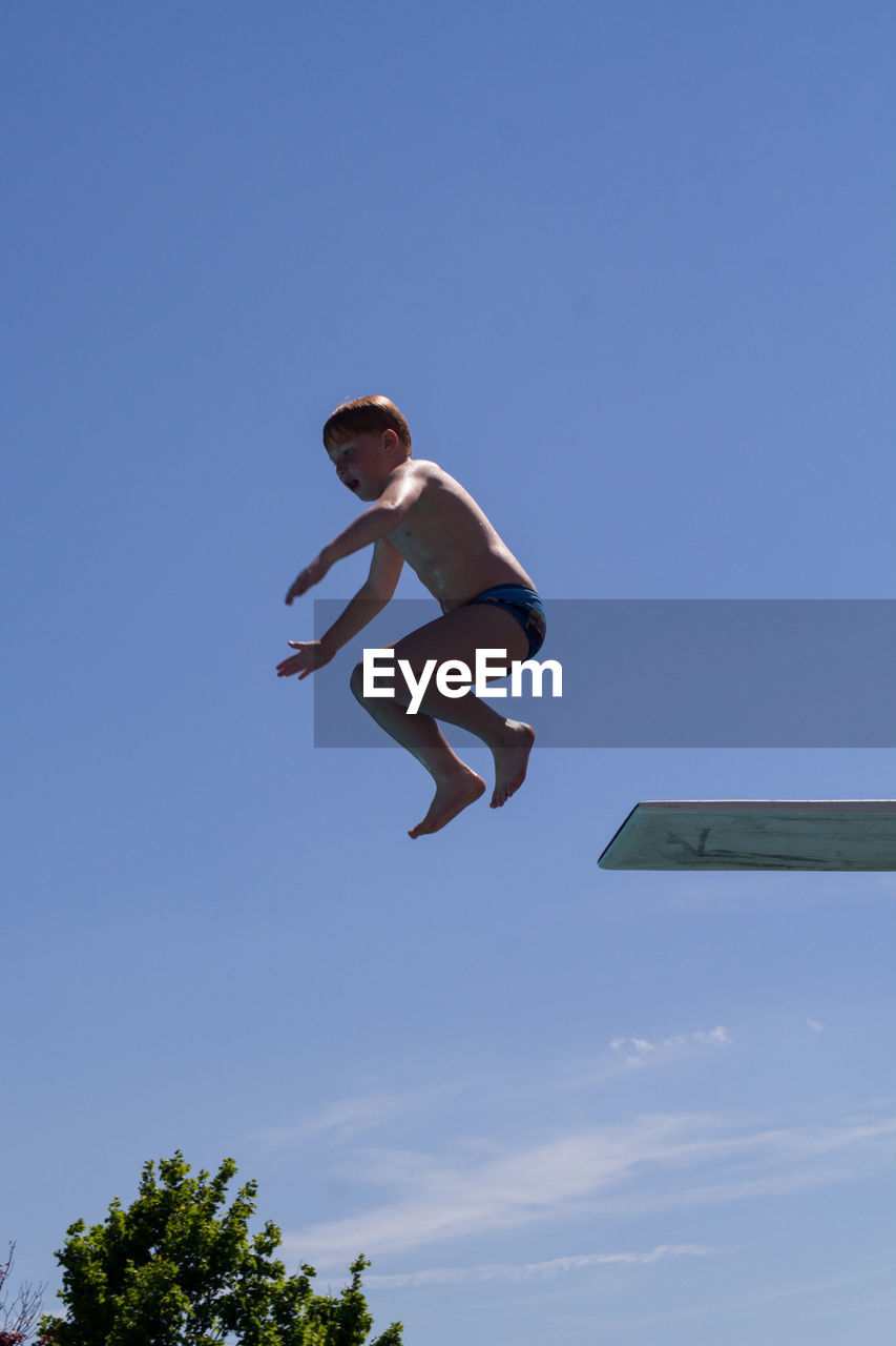 Low angle view of boy jumping from diving board against sky