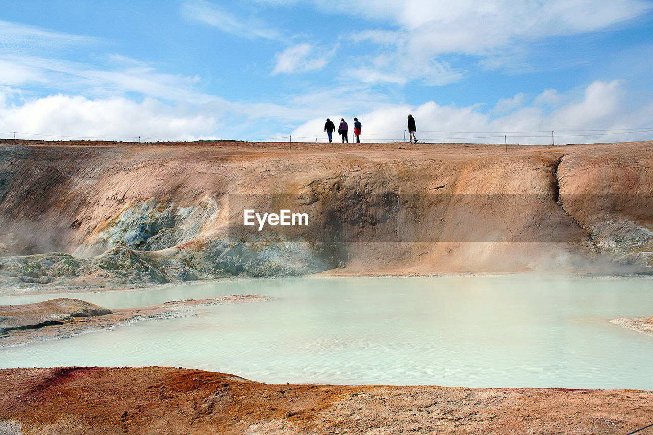 People on rock formation by hot spring against sky
