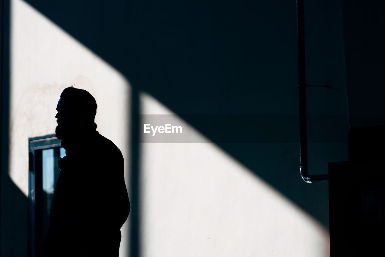 Silhouette hipster man standing against wall