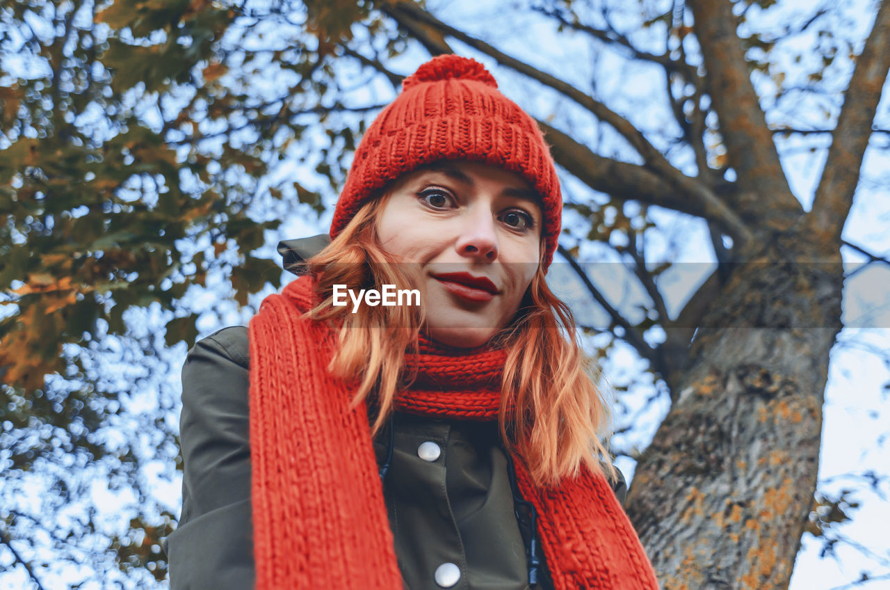 Smiling cute young woman in orange warm knitted hat and scarf. autumn portrait close-up. 