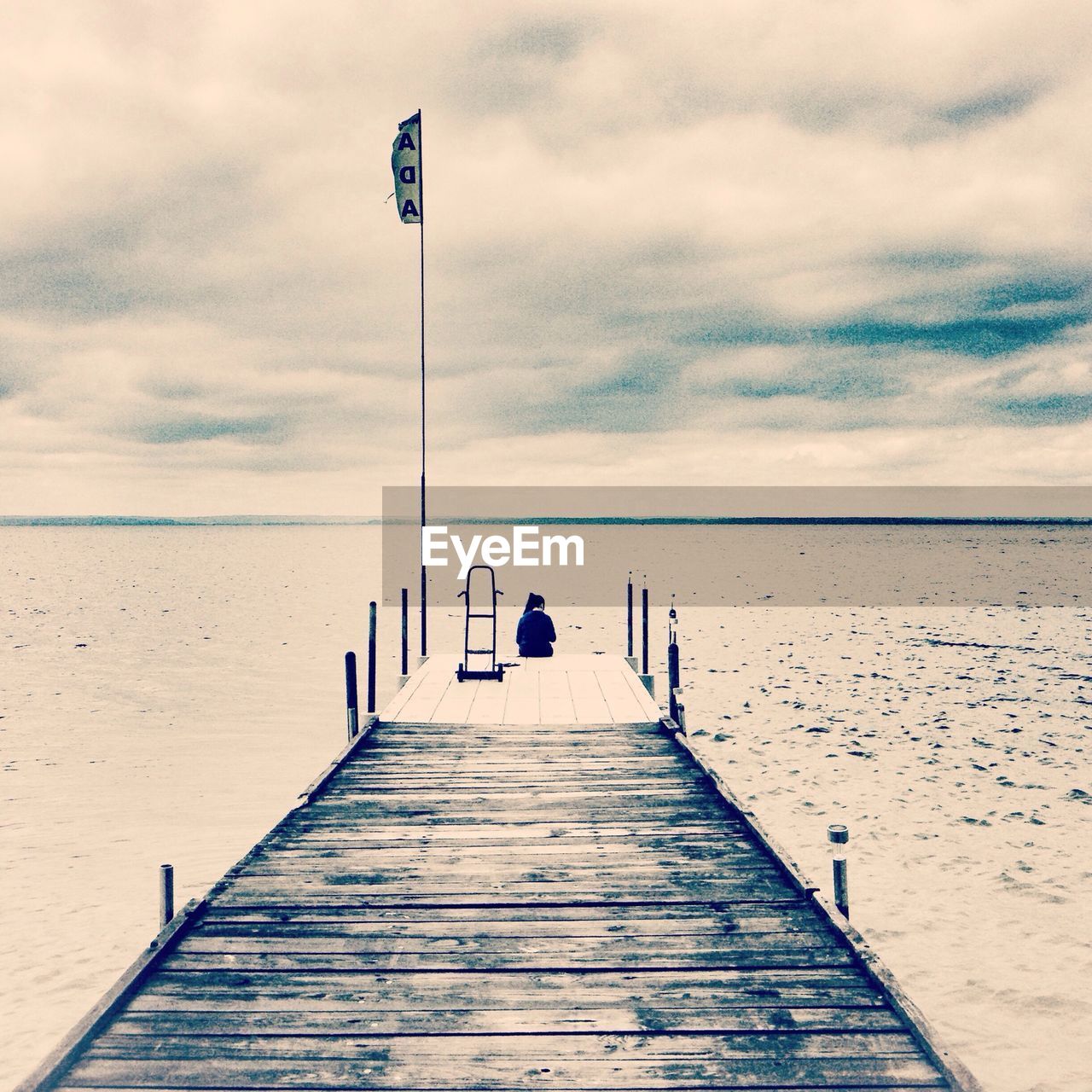 Mid distance shot of a woman sitting on jetty against calm sea