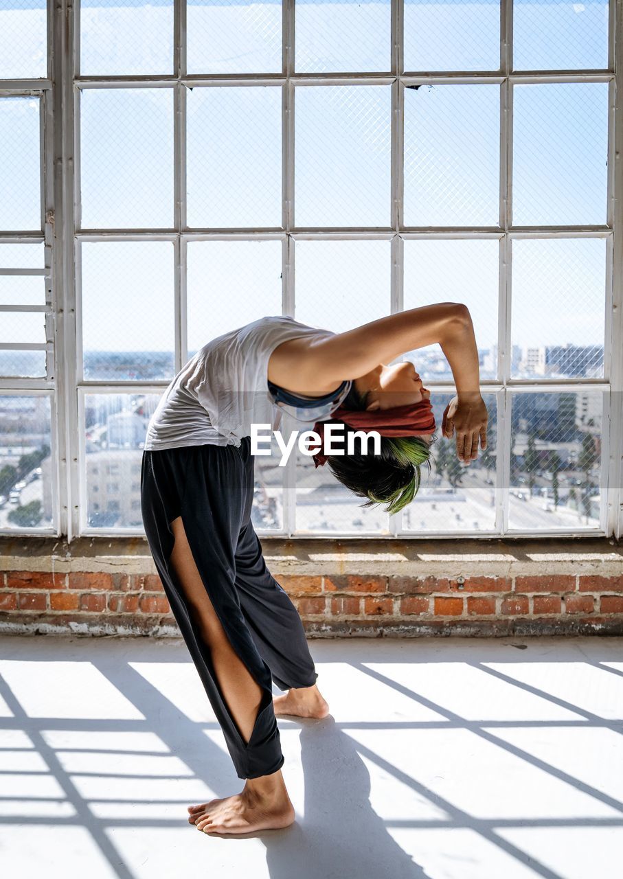 Side view of woman exercising against window