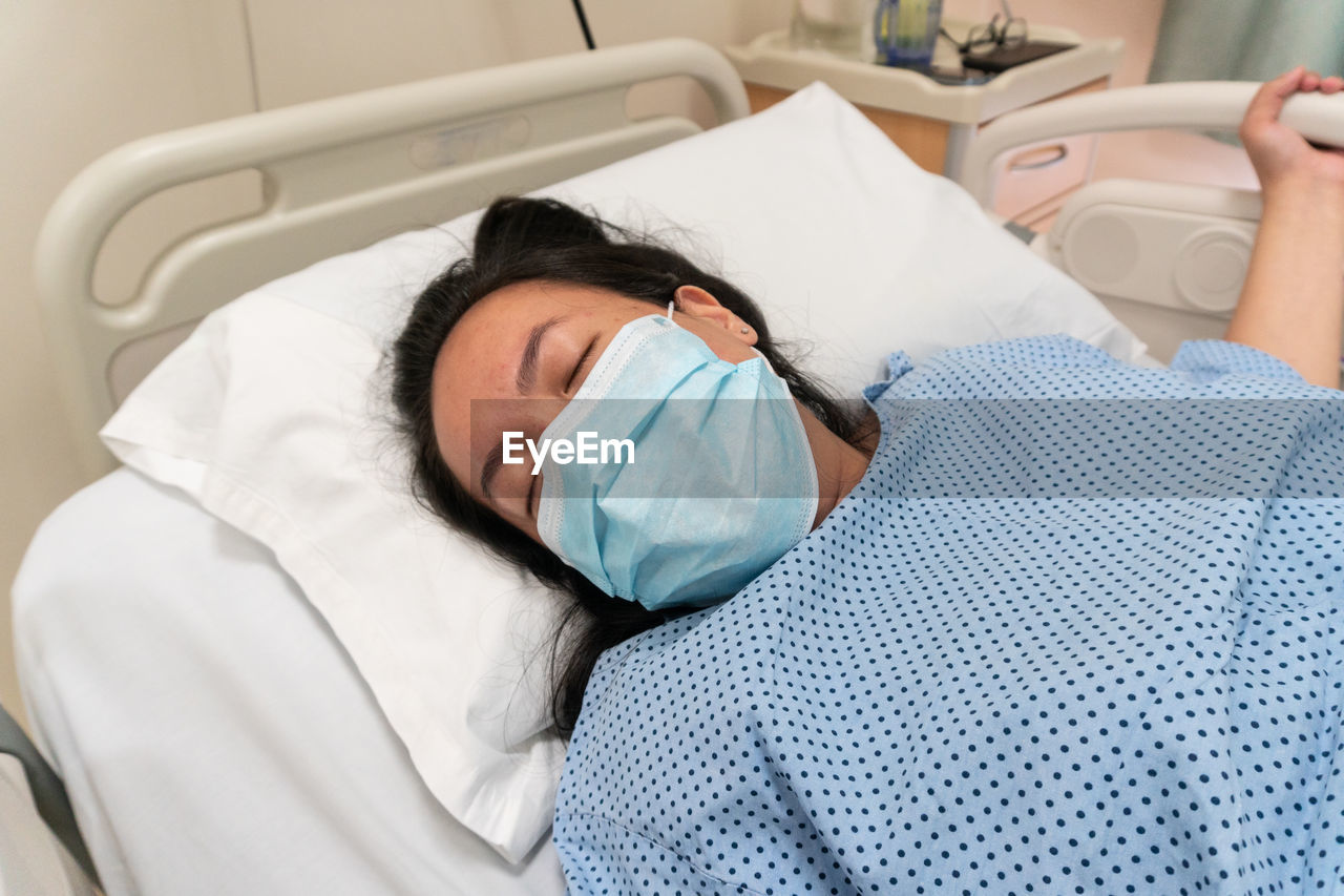 High angle view of woman wearing mask sleeping on bed in hospital