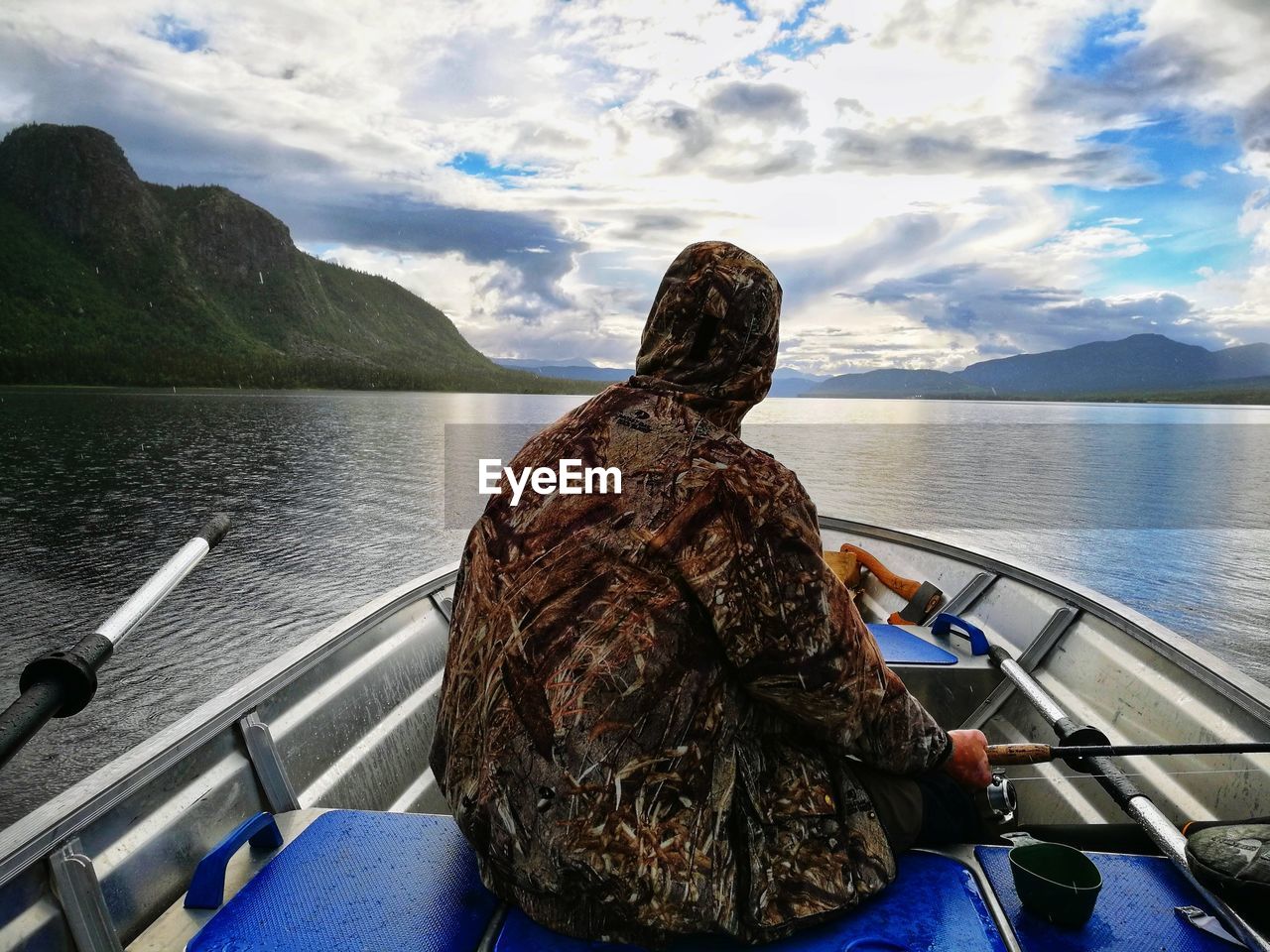 REAR VIEW OF WOMAN SITTING ON BOAT IN SEA AGAINST MOUNTAINS