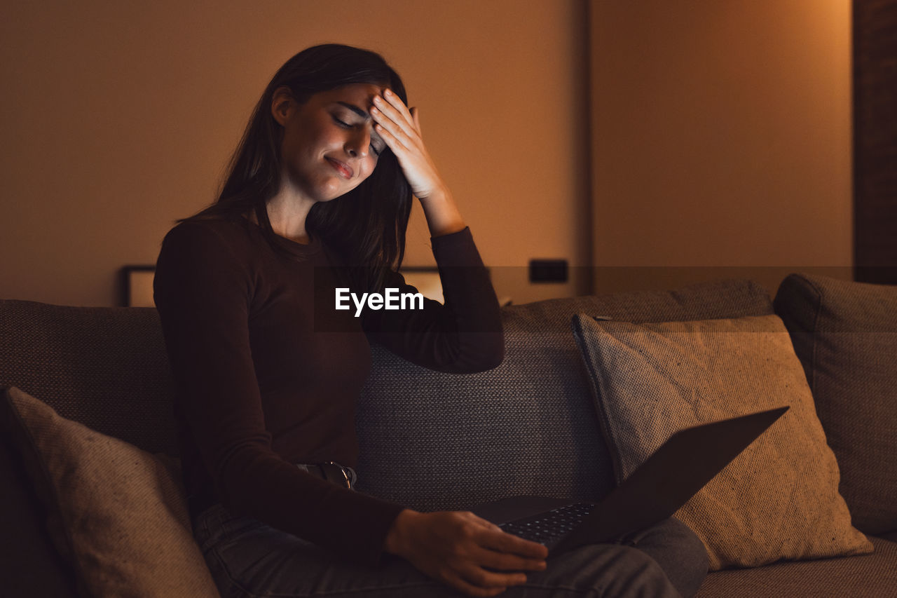 young woman using mobile phone while sitting on sofa at home