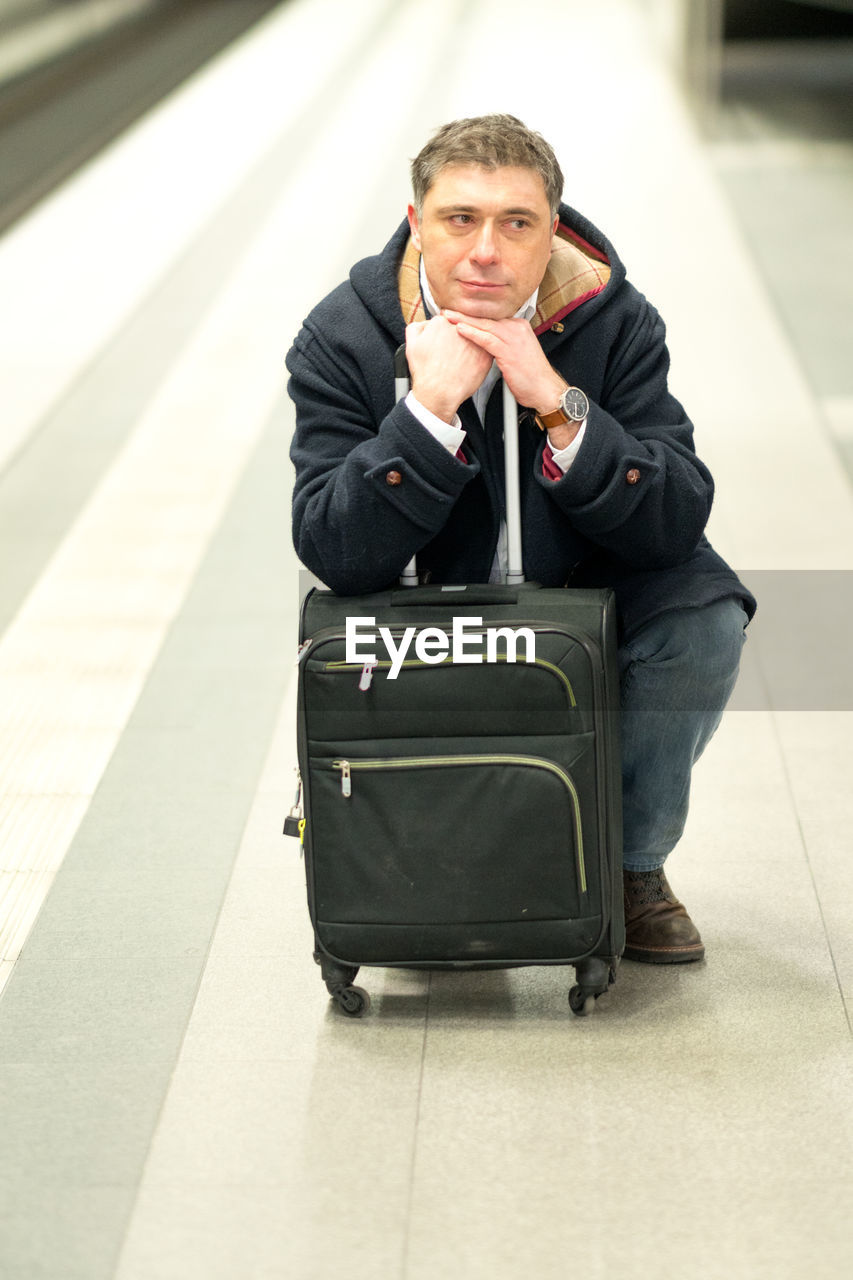 Man with luggage sitting at railroad station platform