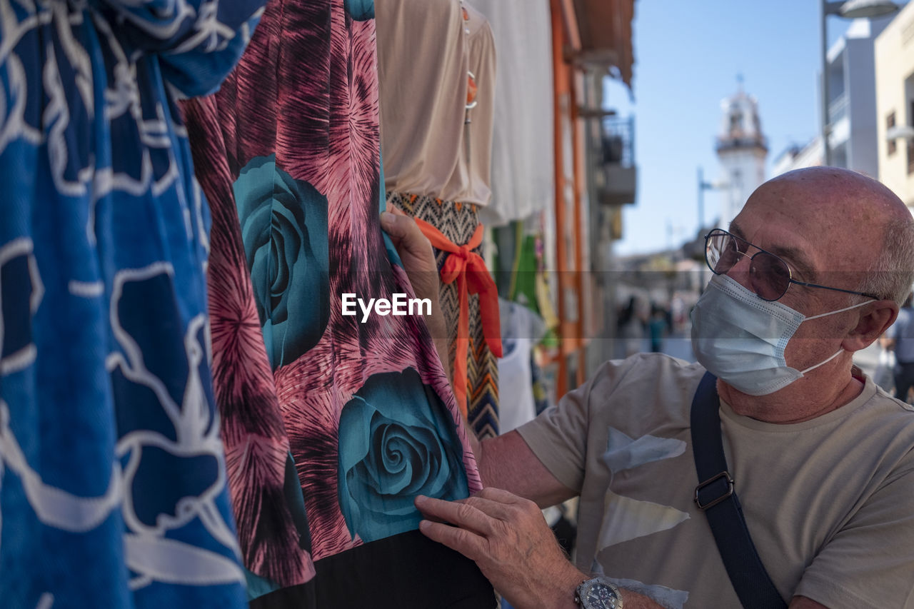 Close-up of senior man wearing mask looking at garment for sale at market