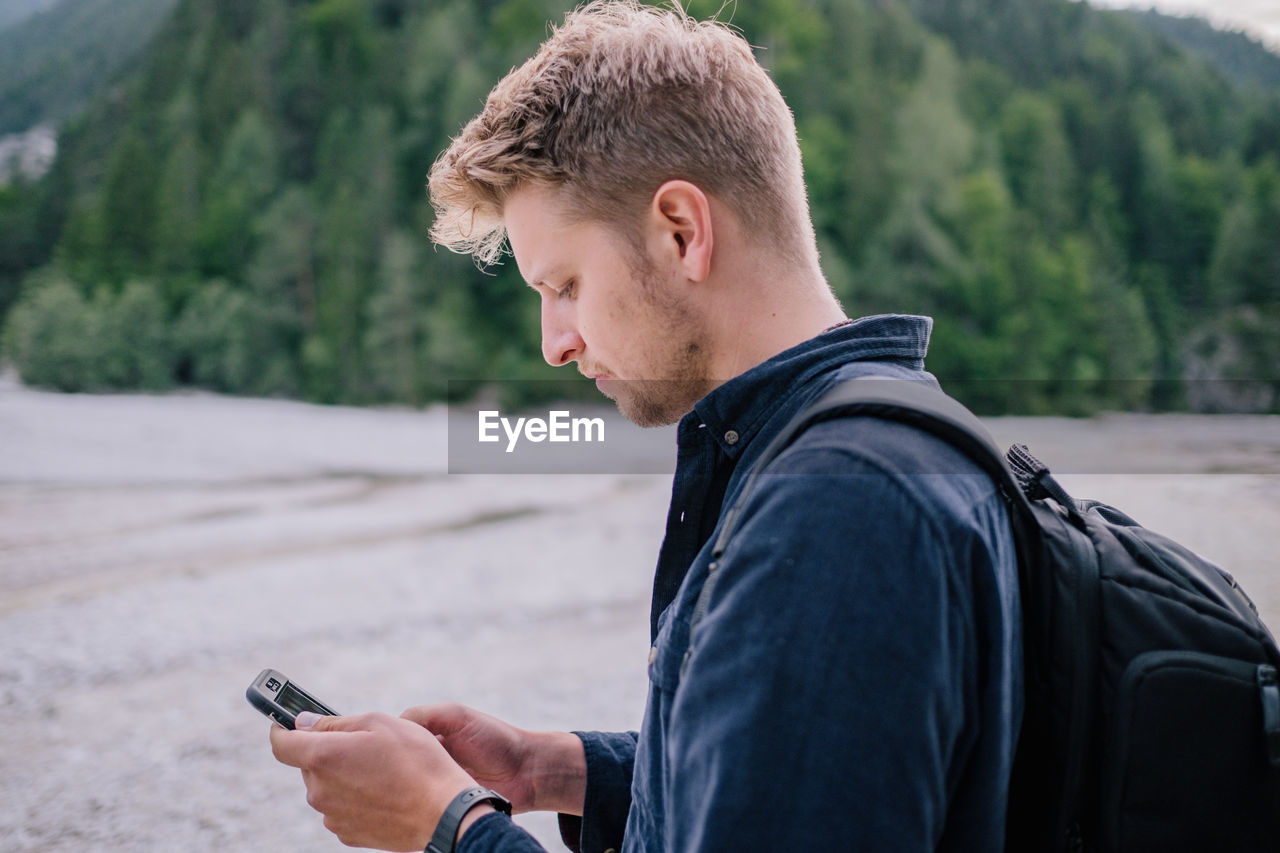 Side view of young man using mobile phone while standing on land