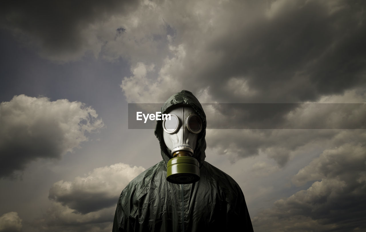 Person wearing gas mask while standing against cloudy sky