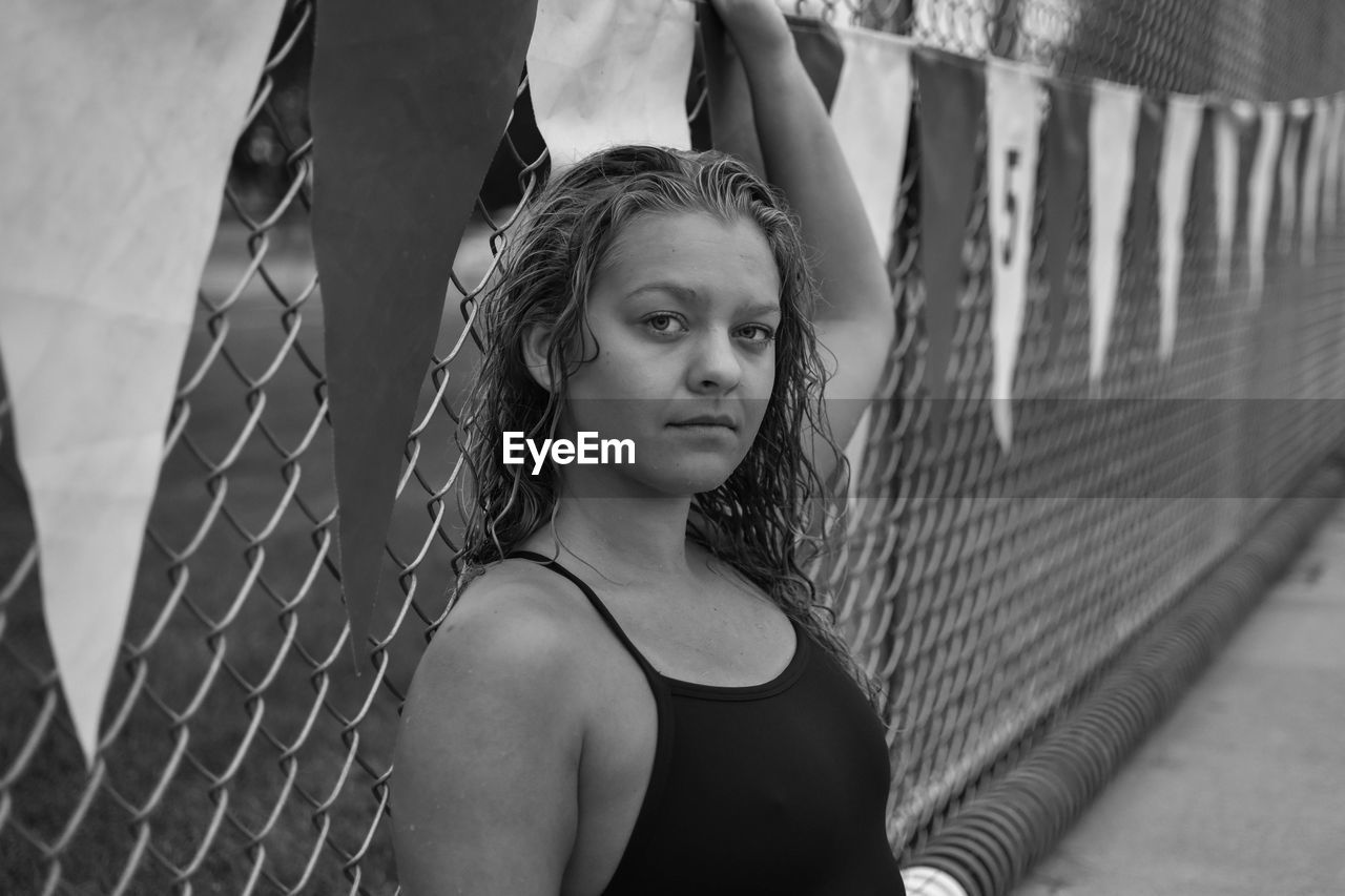 Portrait of young woman in swimwear by chainlink fence