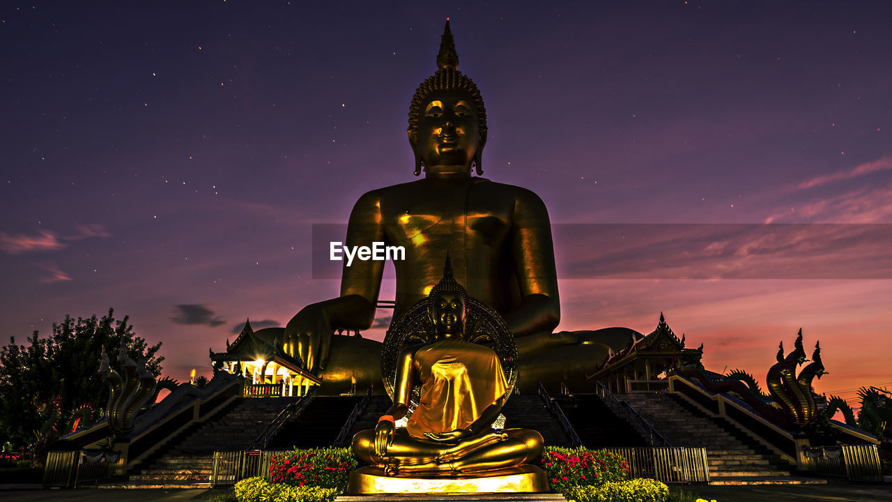 Low angle view of golden buddha statues against star field
