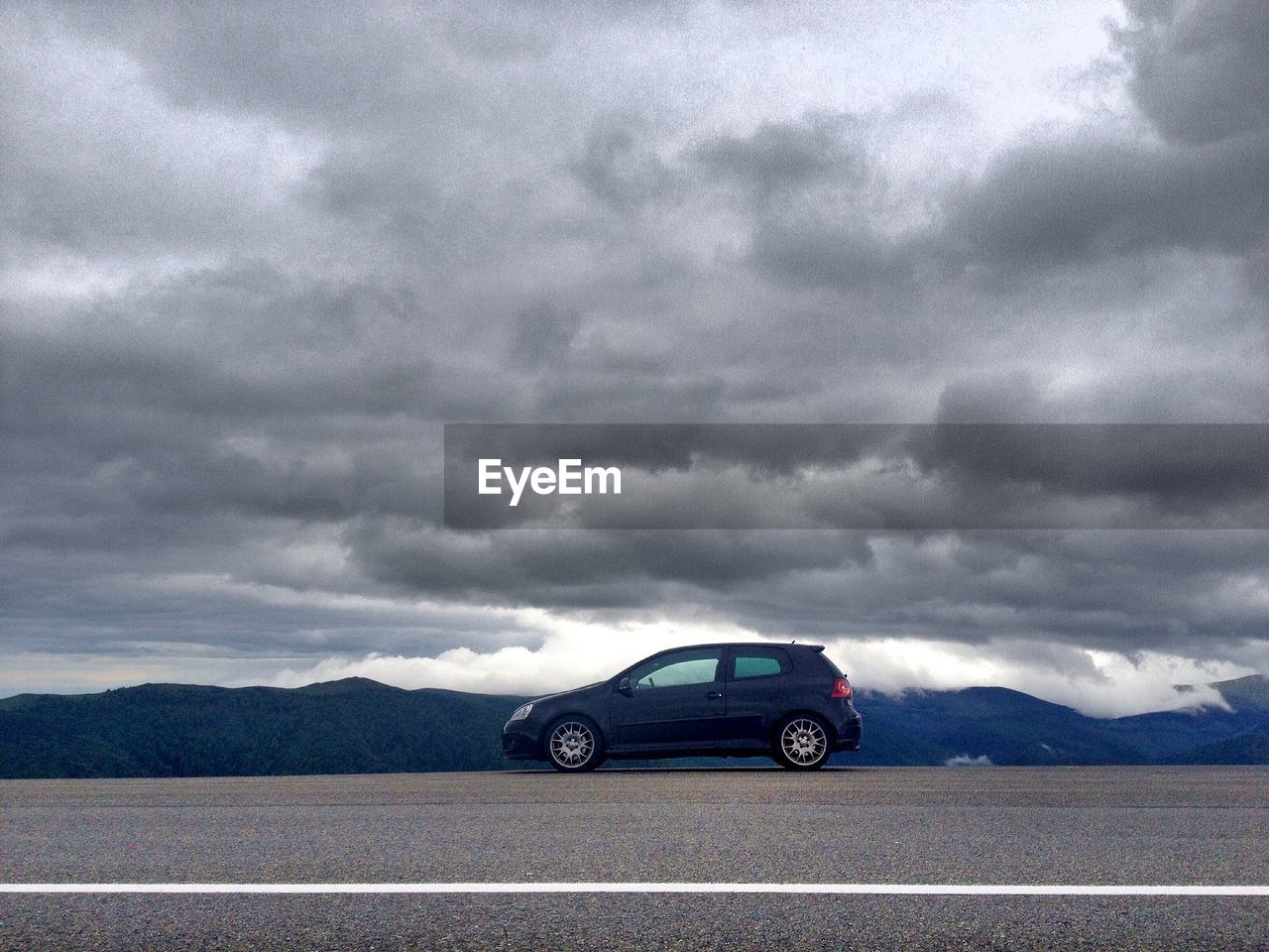 VIEW OF MOUNTAIN ROAD AGAINST CLOUDY SKY