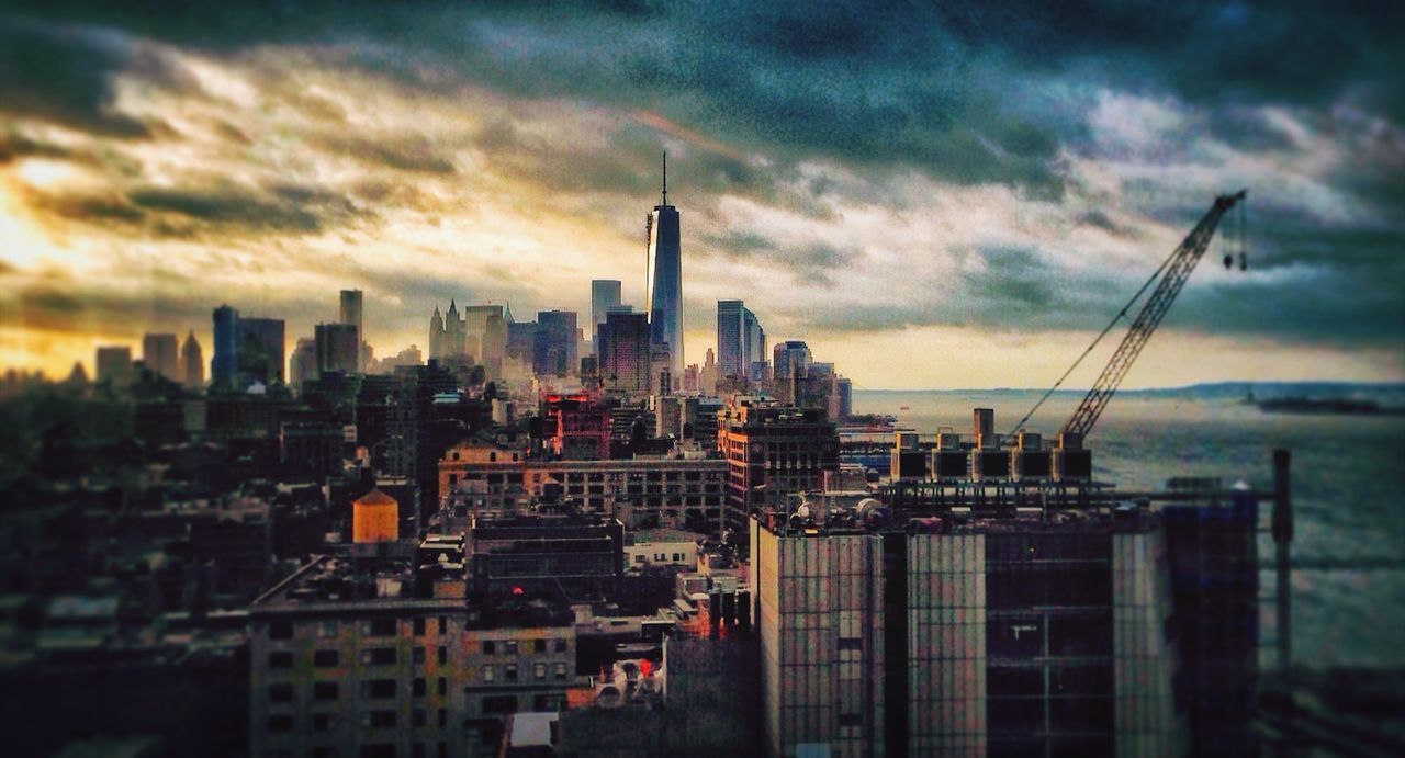 Cityscape with one world trade center by river against cloudy sky during sunset