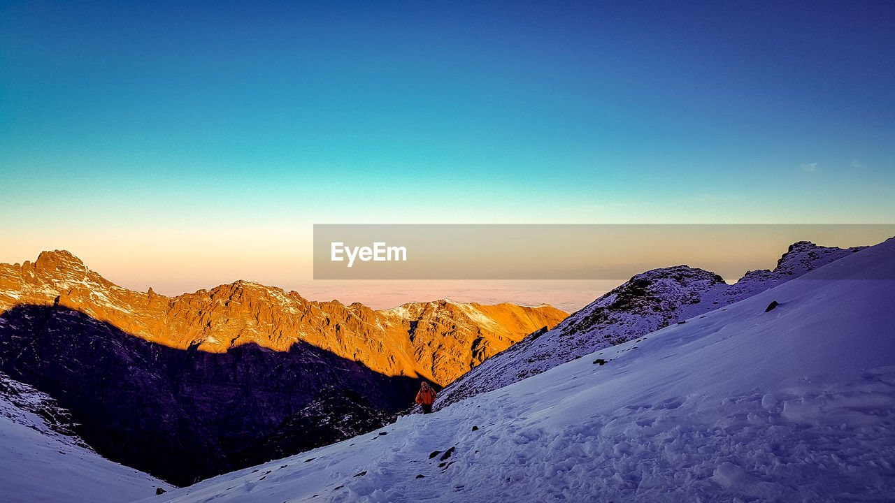 Mid adult woman standing on snowcapped mountain against clear sky during sunset