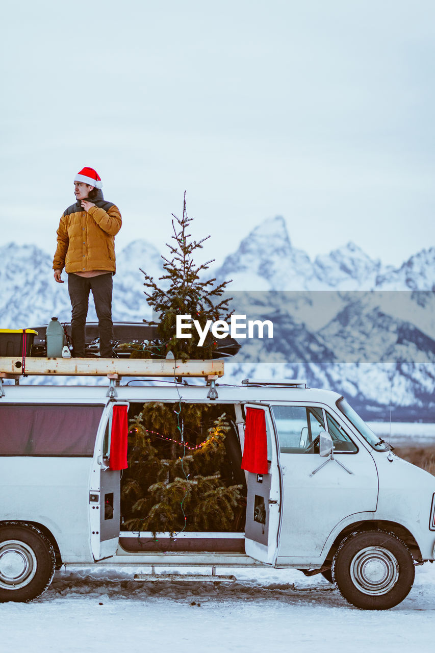 Man stands on top of white passenger van decorated for christmas christmas tree