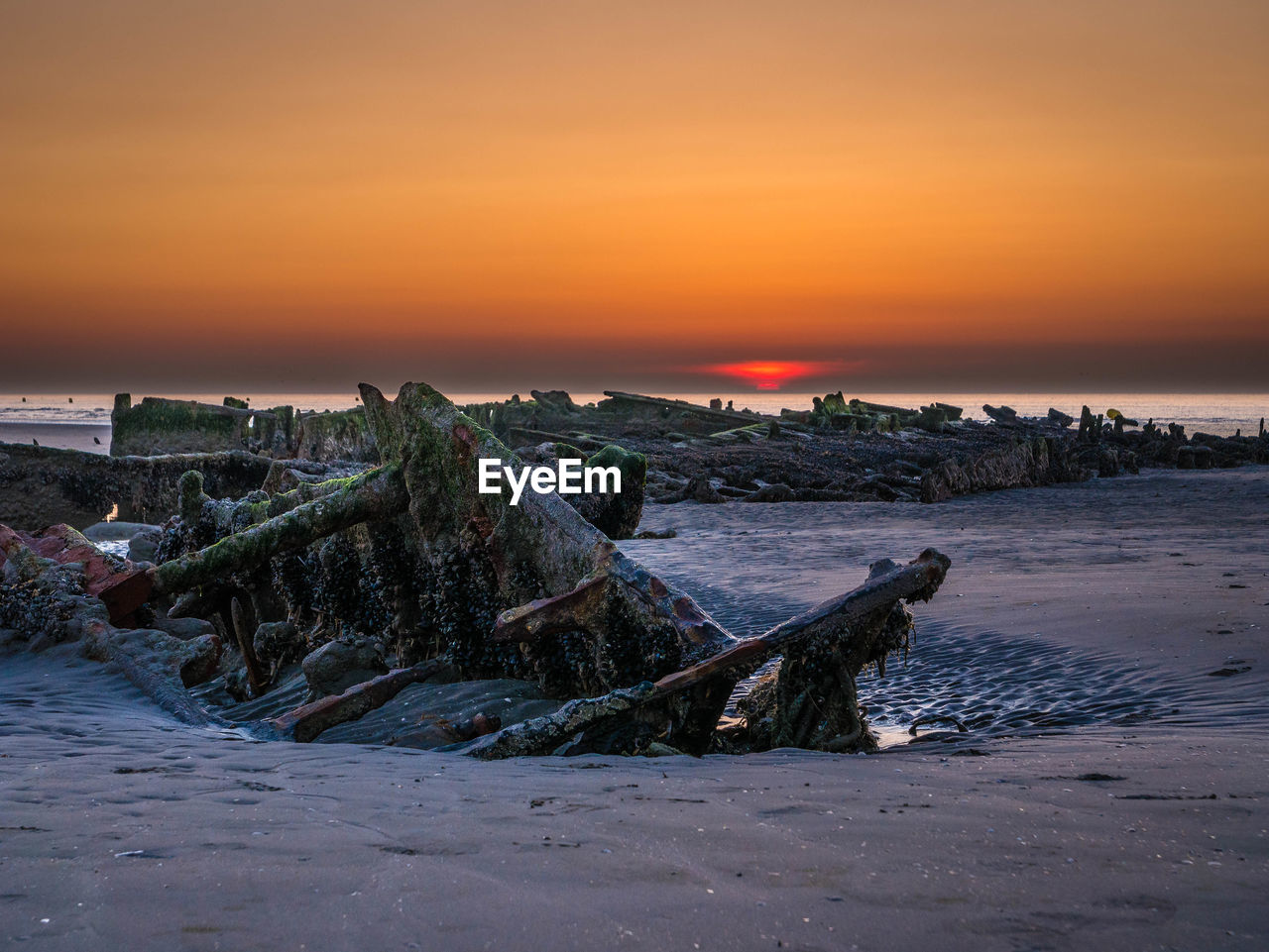 Setting sun behind an exposed shipwreck at low tide from world war ii at the beach
